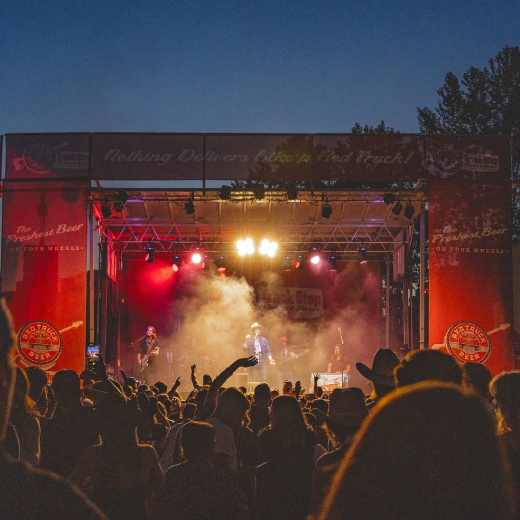 a crowd of people in front of the lit stage at the Red Truck Beer Co Truck Stop Concert Series in Vancouver, BC