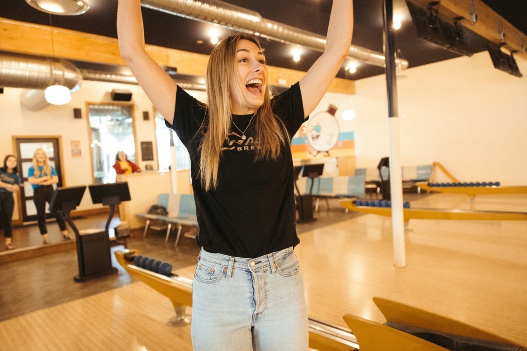 a woman celebrates after bowling her turn at Encore Brewing in Cranbrook, BC