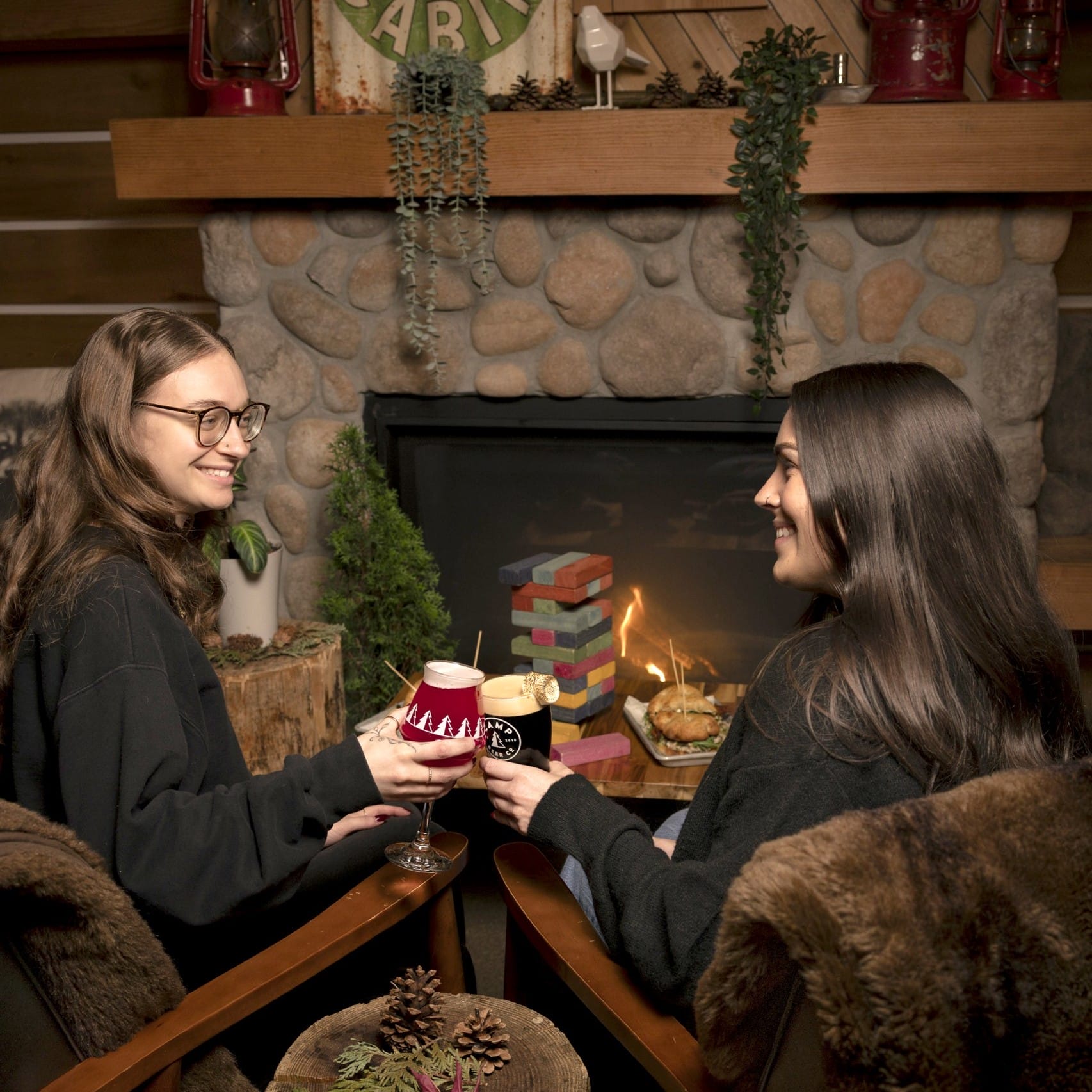 two people relax next to a fire place, with pints of craft beer, a meal and board games at Camp Beer Co in Langley, BC