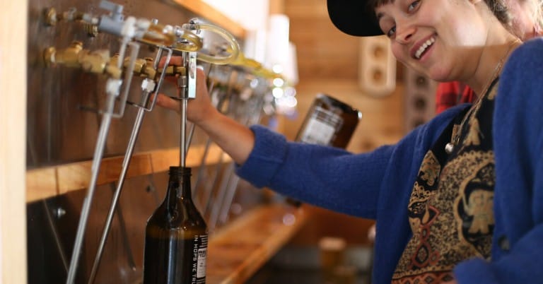 a staff member smiles as they fill a growler at Persephone Brewing on the Sunshine Coast Ale Trail