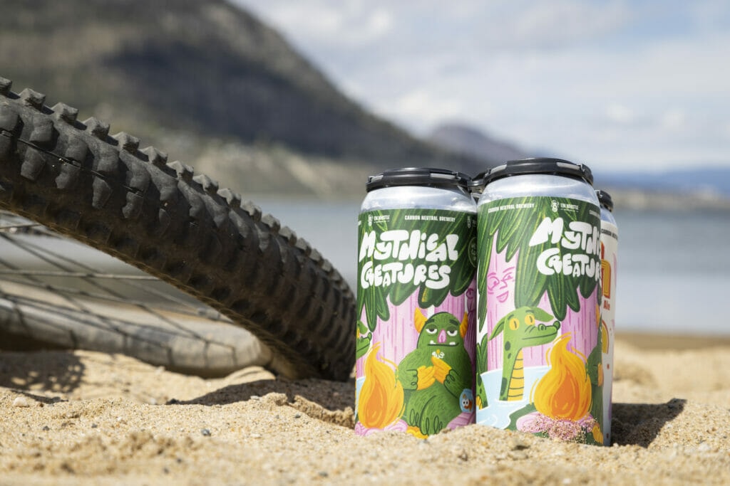 a four-pack of tall cans in the sand next to a mountain bike tire in Penticton, BC