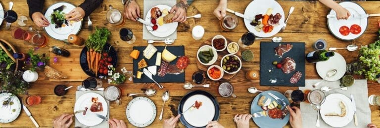 image of wooden table with meats, cheeses, drinks, and people for Hops & Harvest event in Quesnel