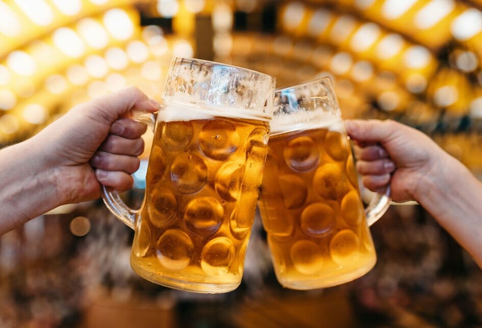 Two large mugs of beer being clinked together in a 'Cheers'