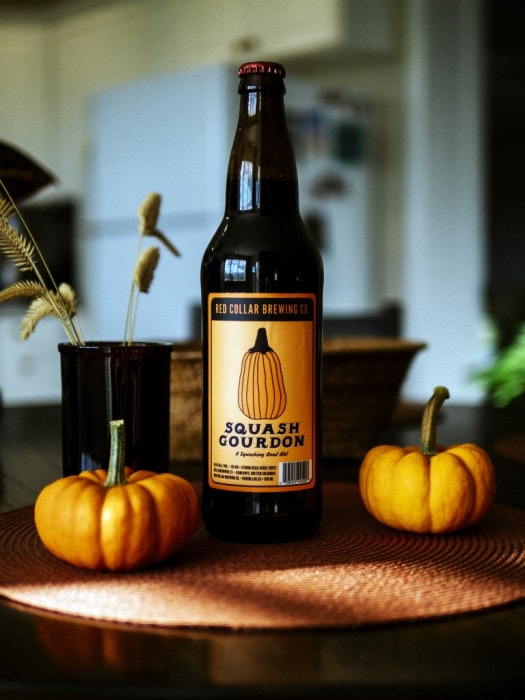 A bottle of Squash Gourdon beer from Red Collar Brewing in Kamloops, BC, surrounded by mini pumpkins