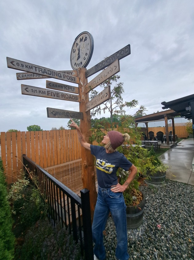 Author Hannah Irvine pointing the way to her next destination at the sign post at Camp Beer Co in Langley BC