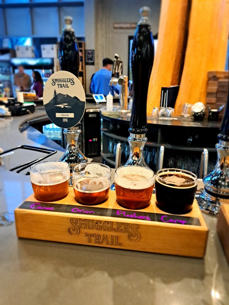 A flight of beer in front of the traditional cask engines at Smugglers' Trail Caskworks in Langley, BC