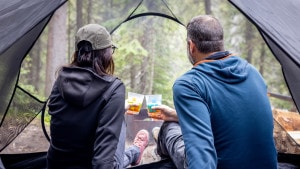 two people enjoy the view from their tent, with beers in hand.