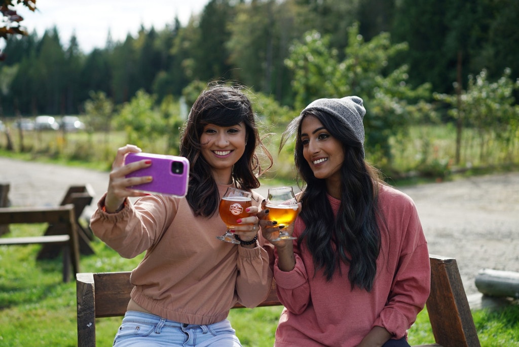 two women take a selfie while holding up pints of craft beer at Persephone Brewing in Gibsons, BC