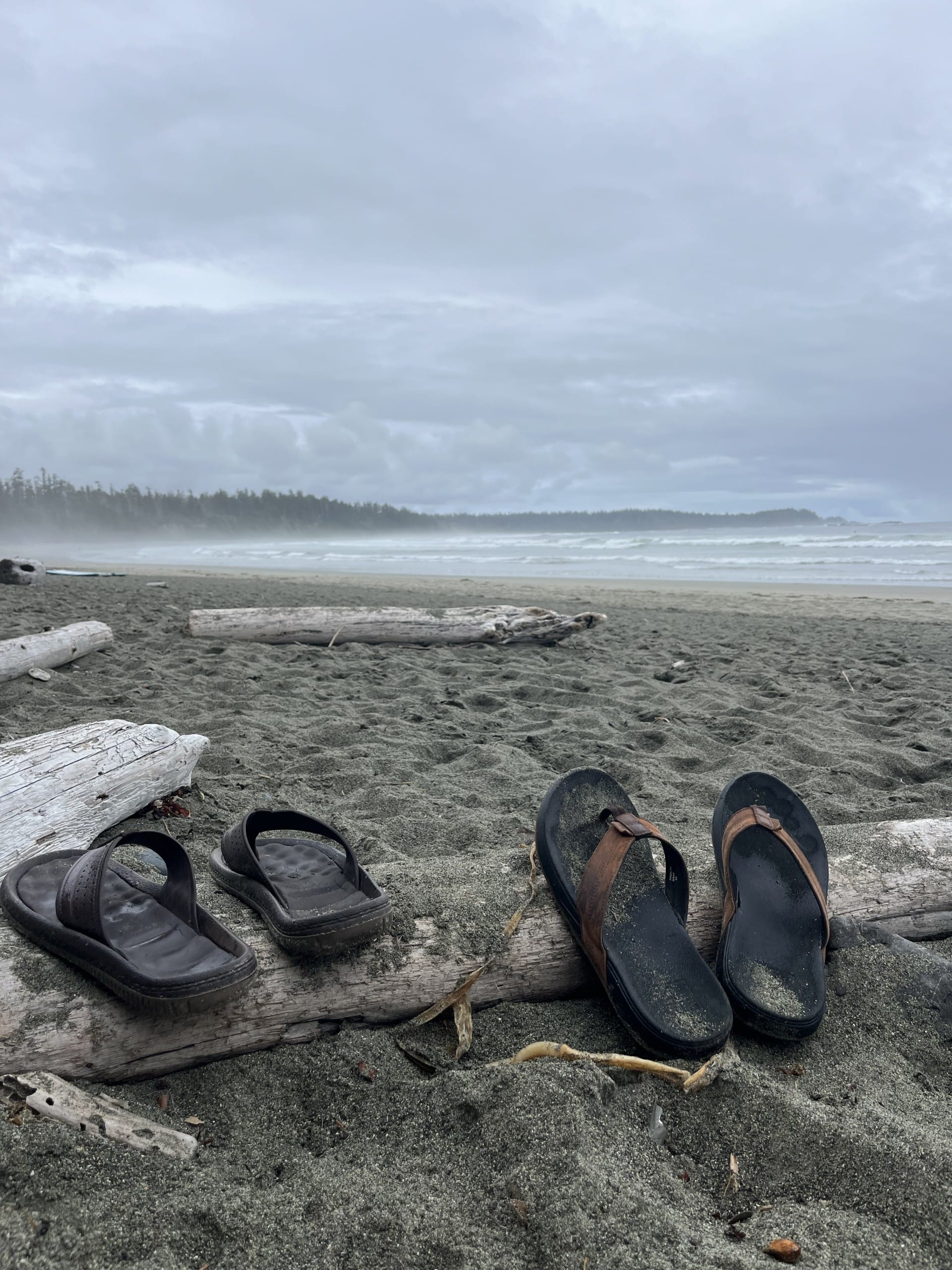 a pair of sandy flip flops sit on the beach with misty waves in the background at Florencia Bay Beach