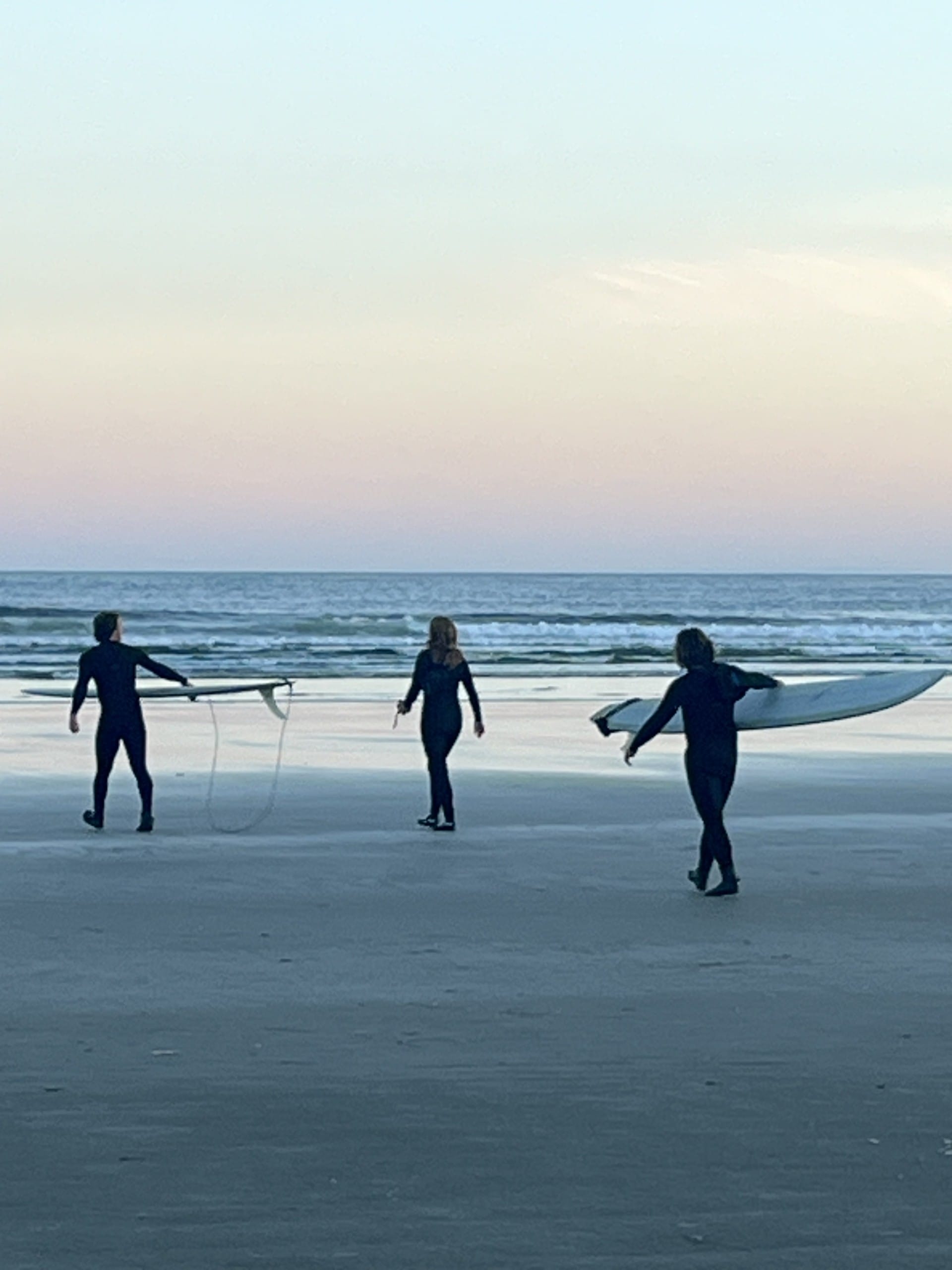 three people in wet suits with surf boards walk along the sand at Florencia Bay Beach