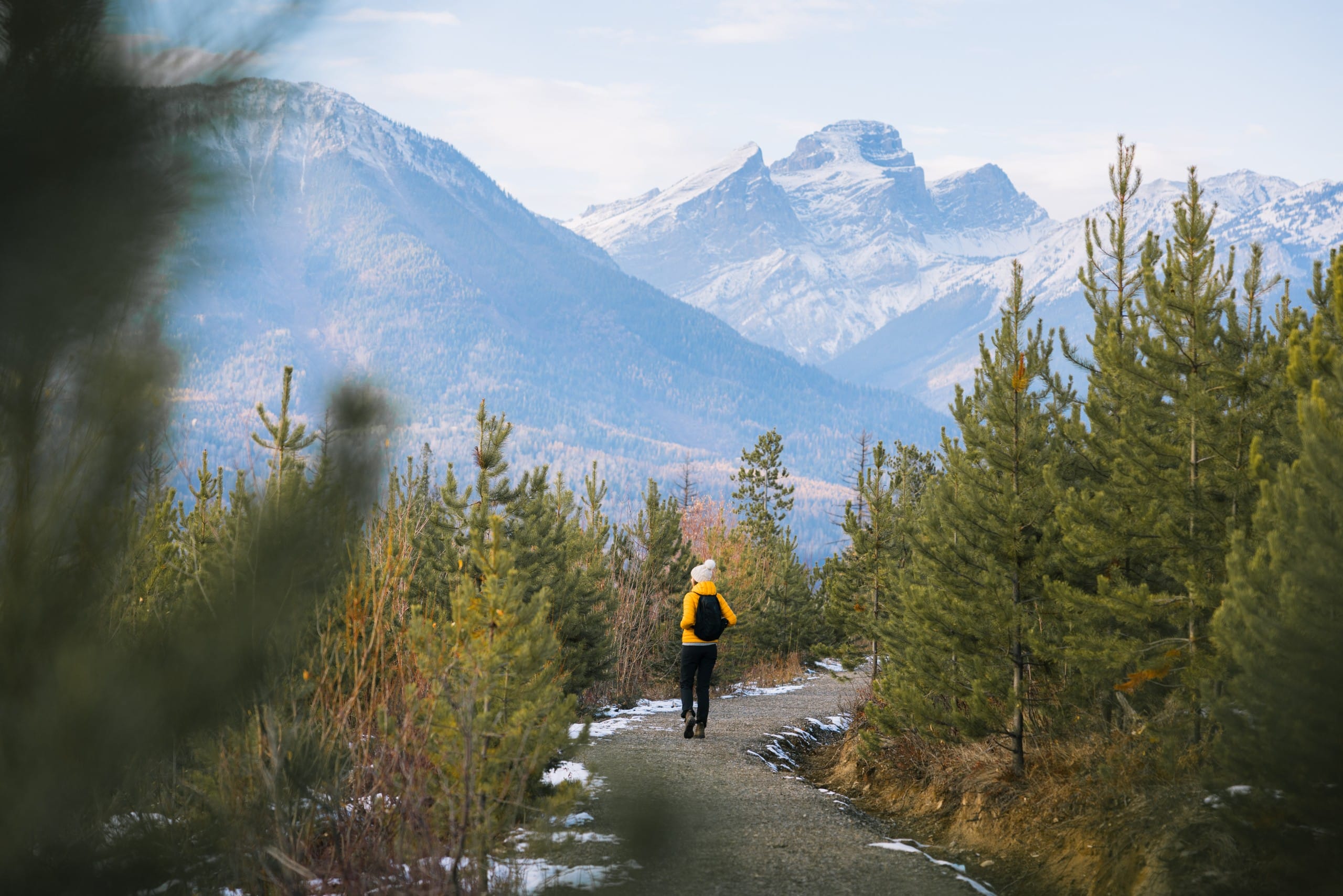 a hiker in a bright yellow jacket pauses on a gravel trail in Fernie, BC