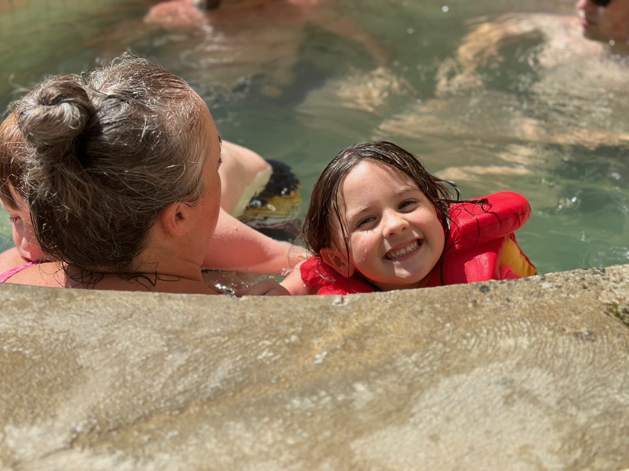 the author's daughter smiling for the camera as she enjoys the hot spring pools with her mom