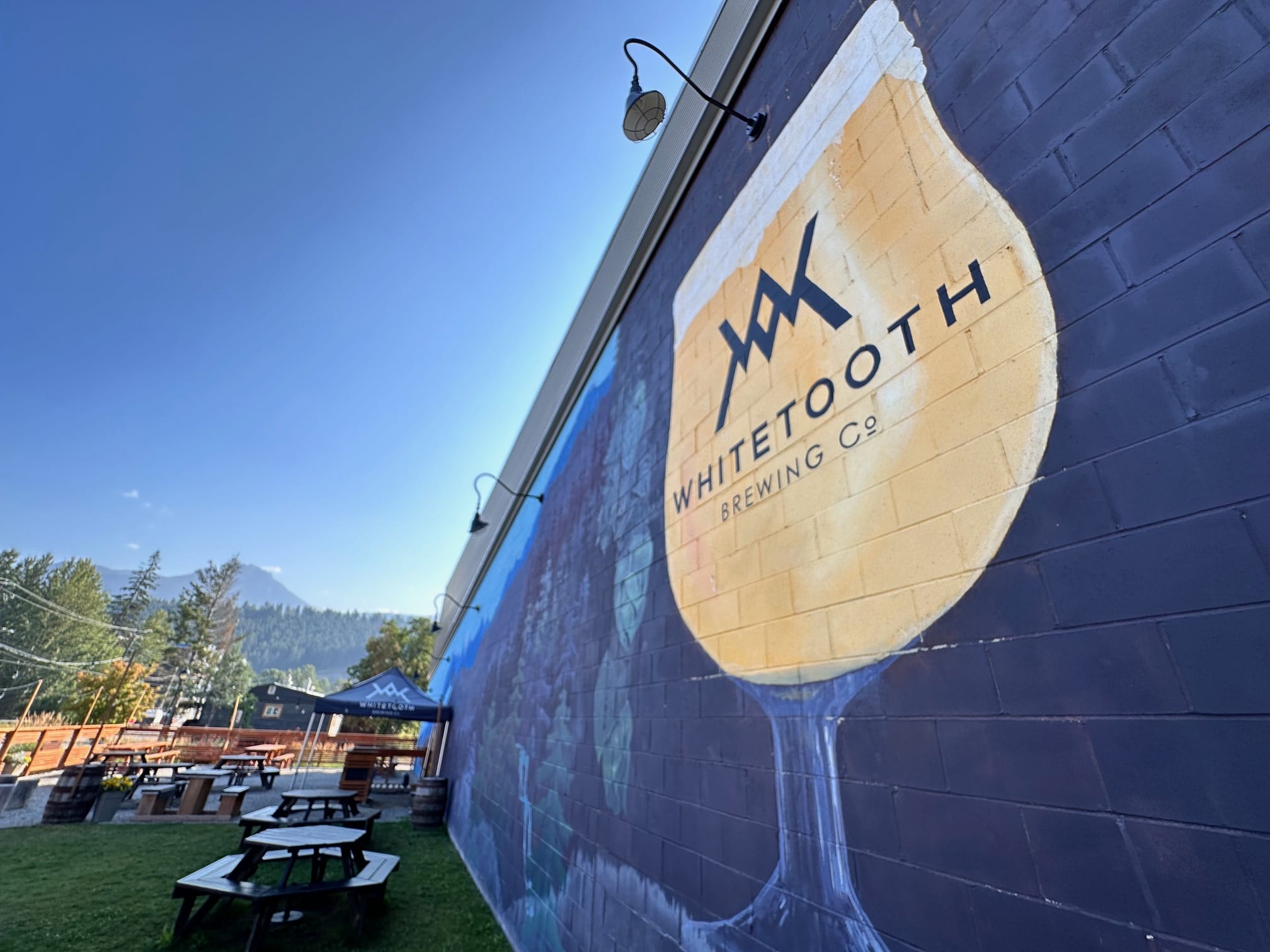 a large mural featuring a branded glass of craft beer covers the side of the brewery next to the patio at Whitetooth Brewing in Golden, BC