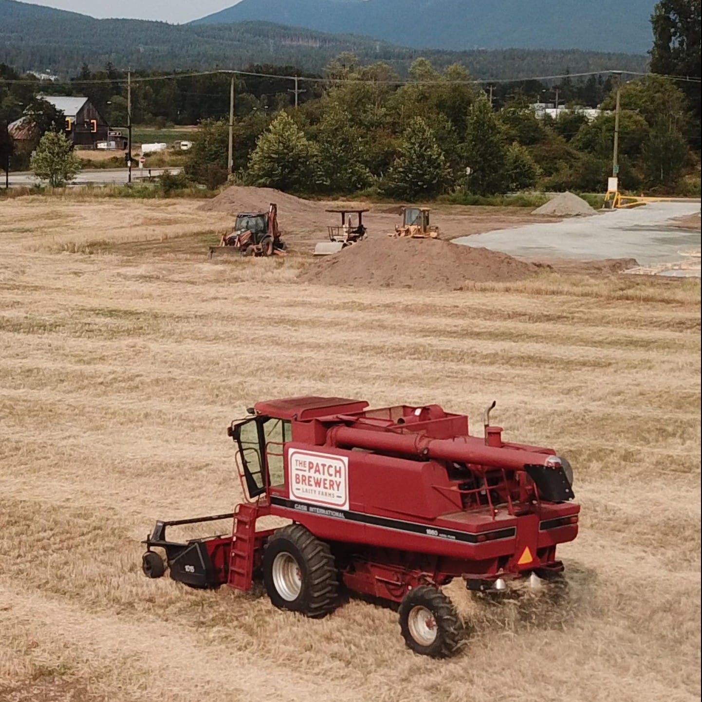 a combine works the barley fields at The Patch Brewery while ground is broken for the brewery's construction in the background