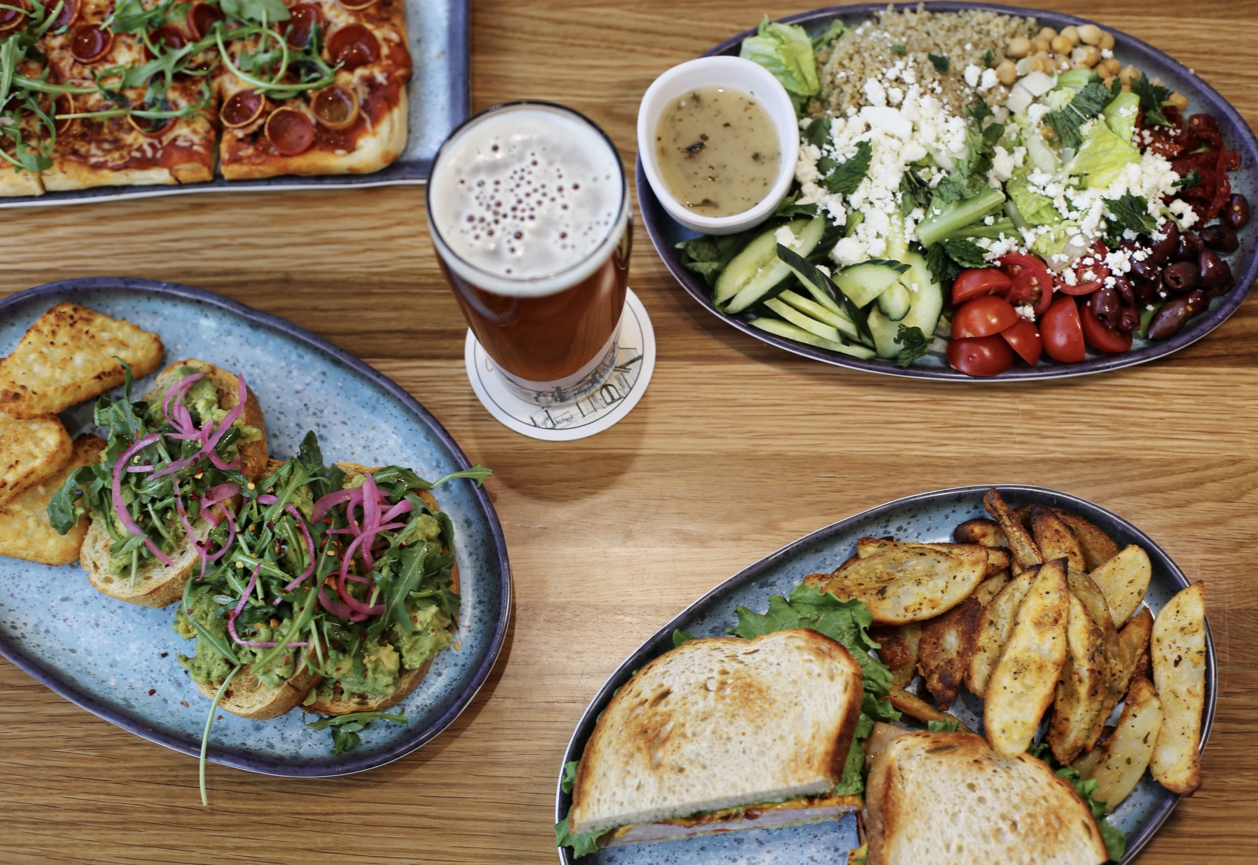 several dishes of freshly prepared food surround a glass of local craft beer at Ellison Field Taphouse at Kelowna International Airport 