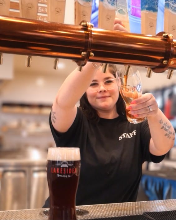 a smiling staff member pours a pints of craft beer at Lakesider Brewing Co. in West Kelowna, BC