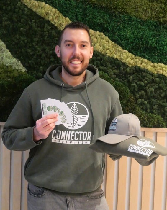 a staff member holds up gift cards and merch at Connector Brewing in West Kelowna, BC - perfect for holiday gift-giving