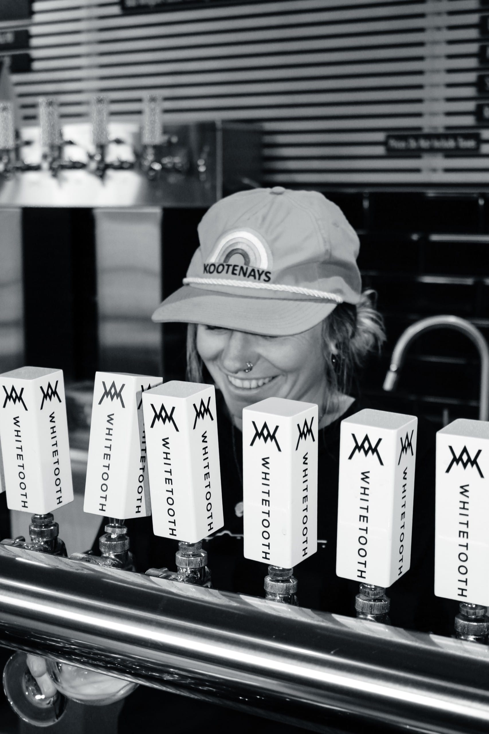 a black and white photo of a smiling staff member behind the taps at Whitetooth Brewing in Golden, BC
